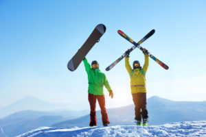 Ein Snowboarder und ein Schifahrer halten ihre Board und Schi in die Höhe.