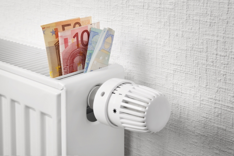 Das Bild zeigt einen weißen Heizkörper mit zusammengefalteten Euro-Banknoten als Symbol für den Energiekostenzuschuss