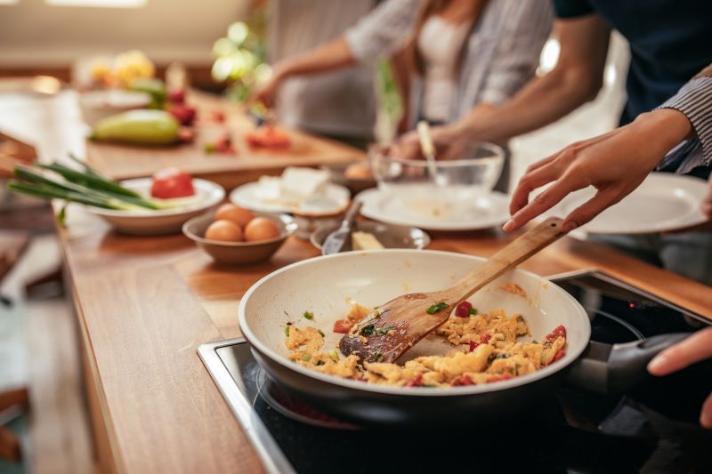 auf einer Theke stehen Schüsseln mit Lebensmittel, mehrere Personen kochen gemeinsam