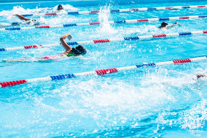 mehrere Athletinnen schwimmen in Bahnen im Kraulstil. Die Bahnen sind durch rot-weiß-blaue Abtrennungen gekennzeichnet.